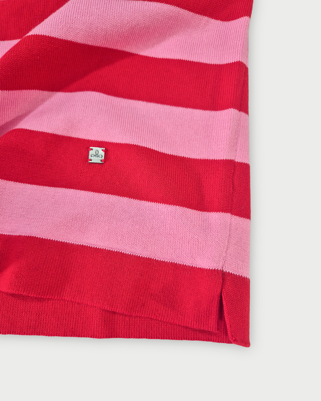 Dettaglio fondo maglia donna in cotone con girocollo e righe rosse e rosa su sfondo bianco