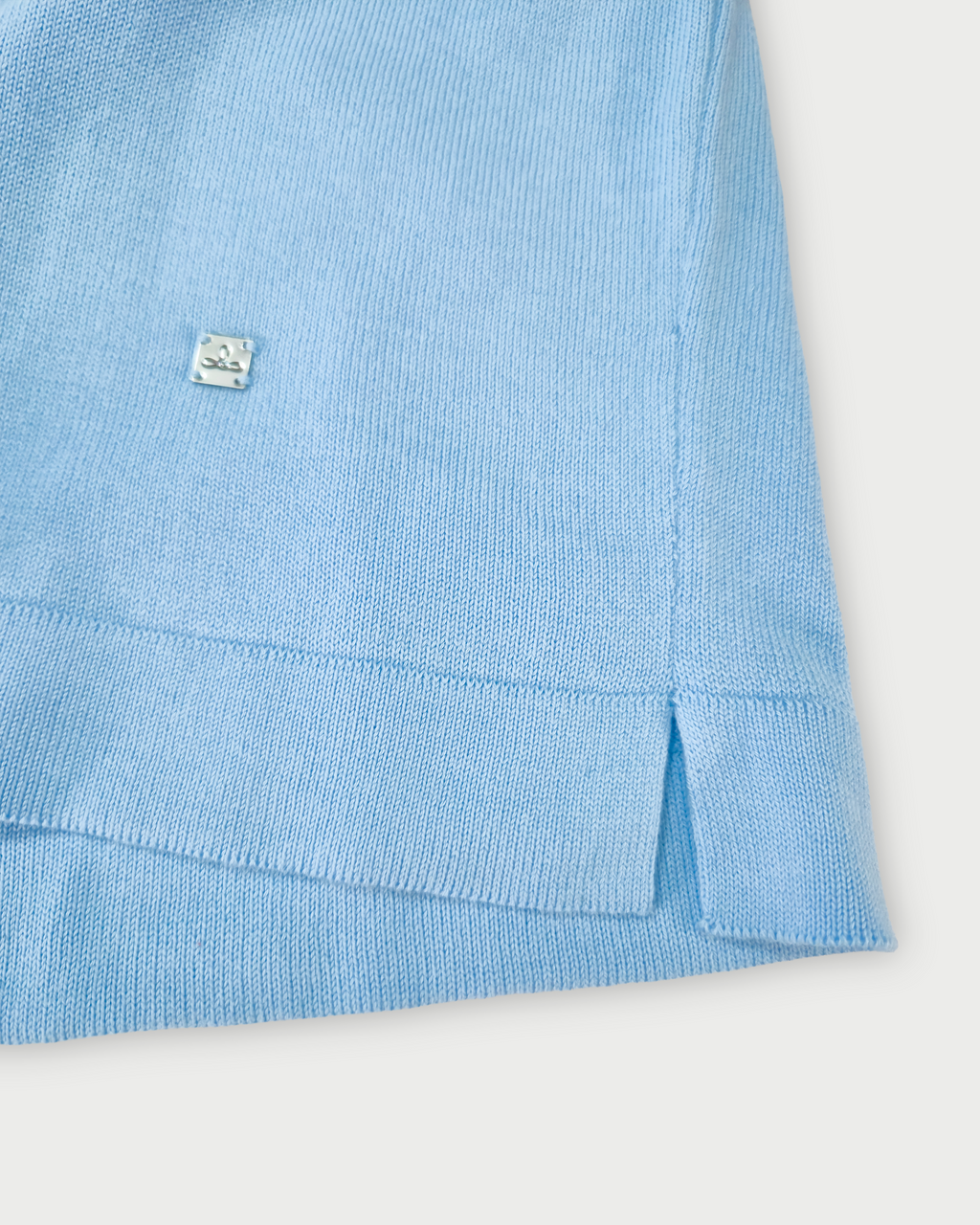 Dettaglio fondo maglia donna in maglia di cotone celeste con scollo a V e profilo blu su sfondo bianco