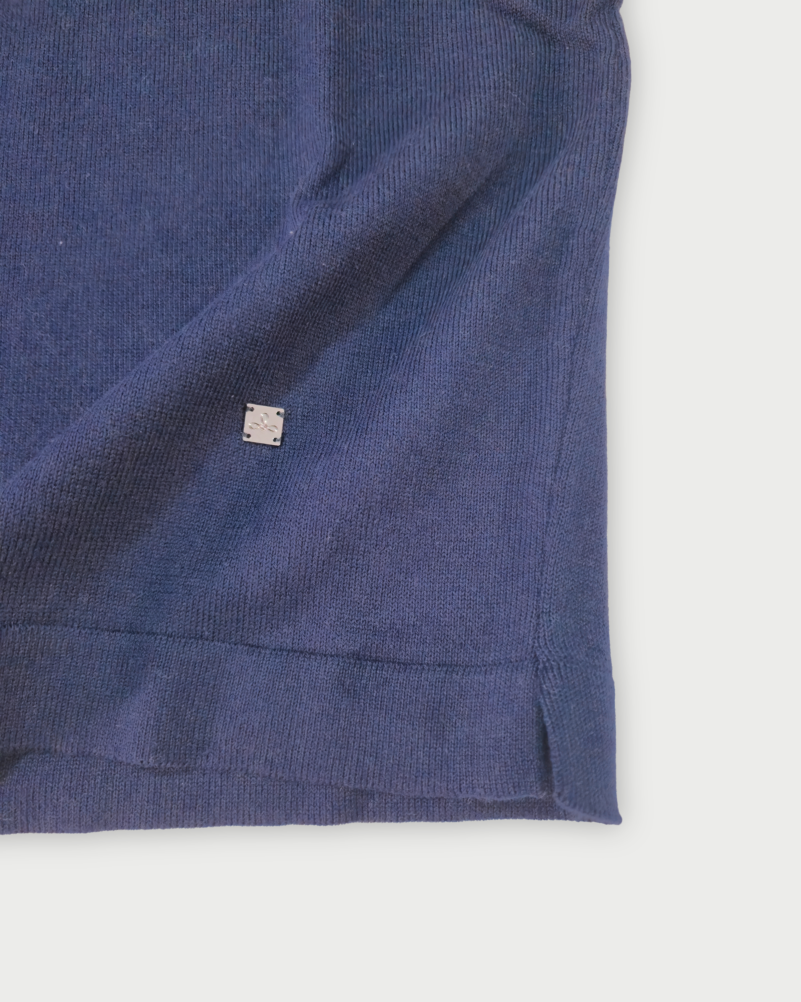 Dettaglio del fondo della maglia donna in cotone blu con scollo a V e profilo bianco su sfondo bianco