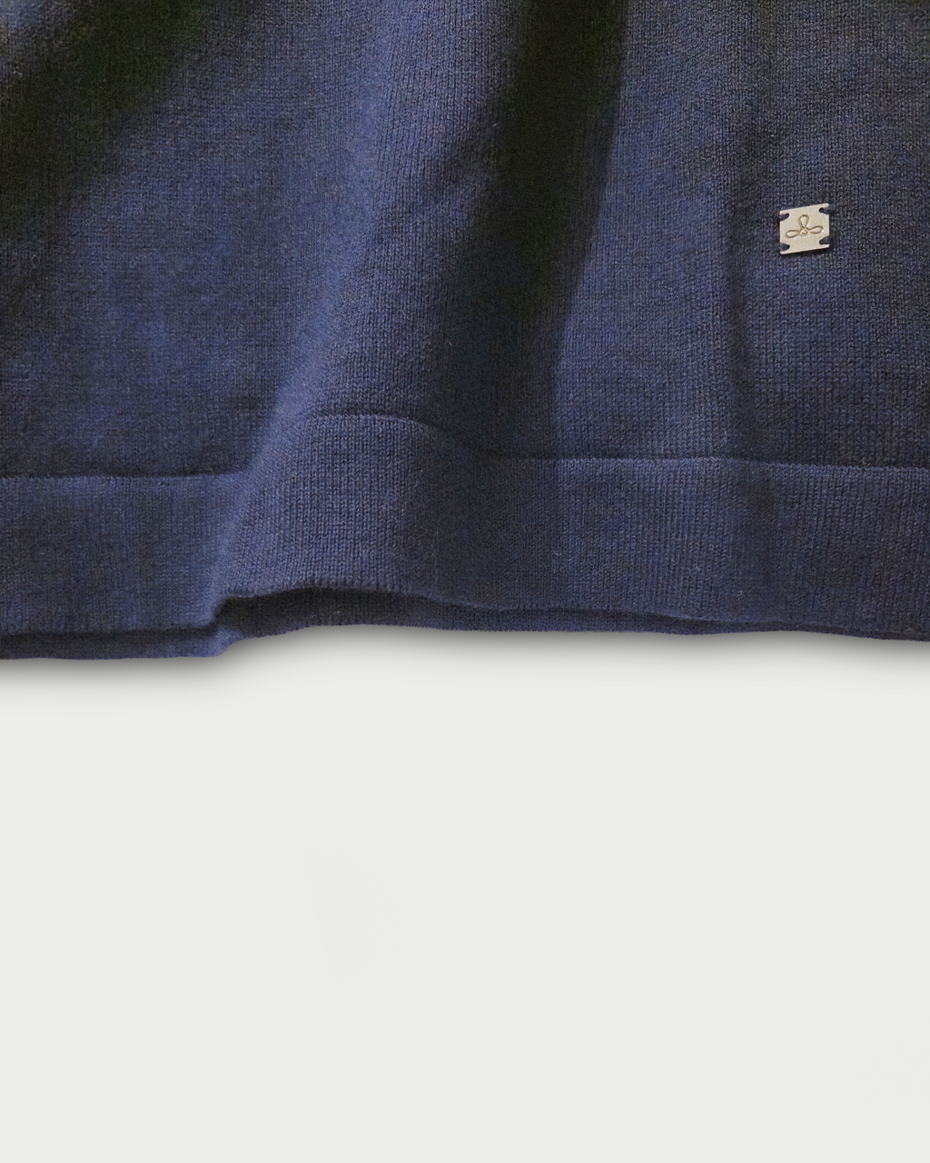 Dettaglio del fondo con logo Edua della polo donna over in maglia di cotone blu su sfondo bianco
