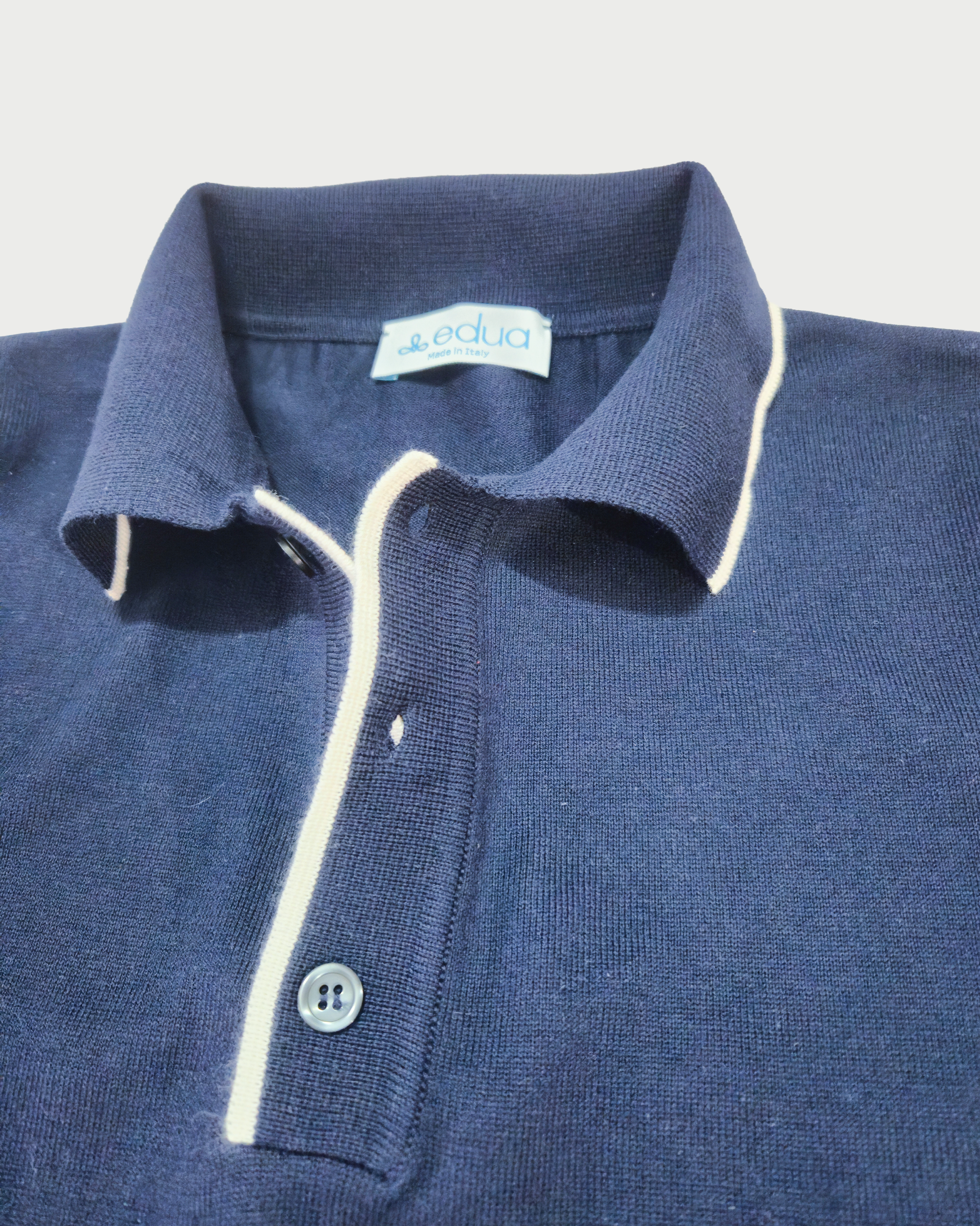 Dettaglio colletto polo maniche lunghe uomo in maglia di cotone blu su sfondo bianco