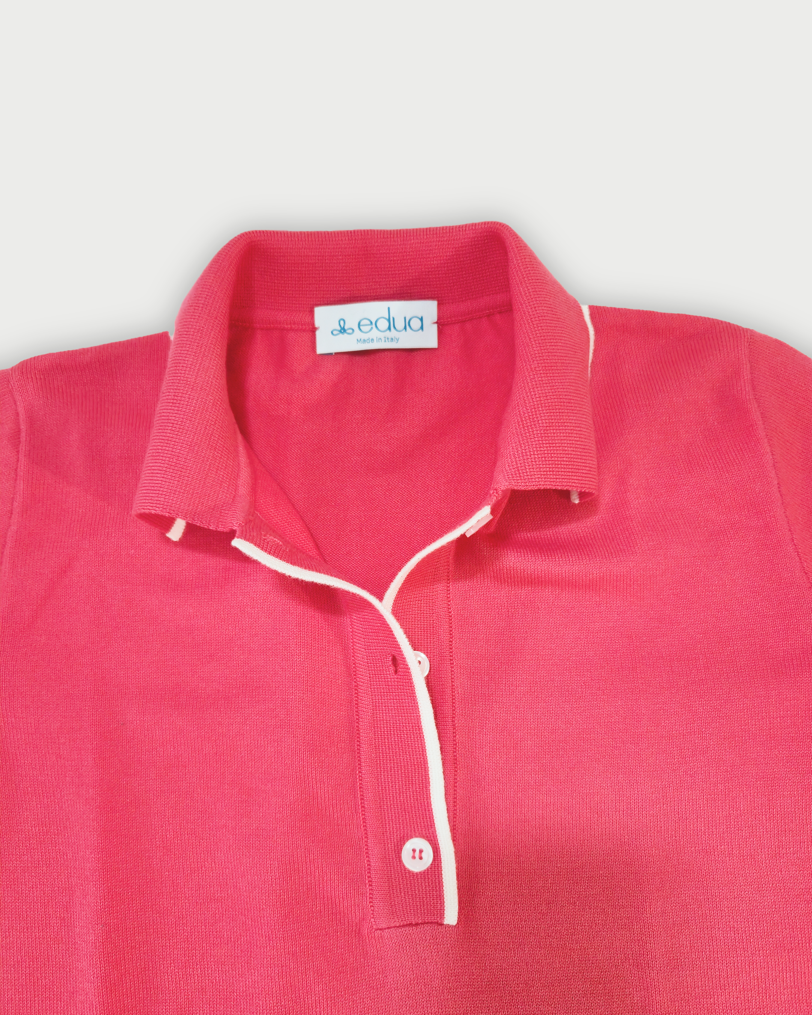 Dettaglio del colletto della polo donna rosa corallo con bordi bianchi su sfondo bianco
