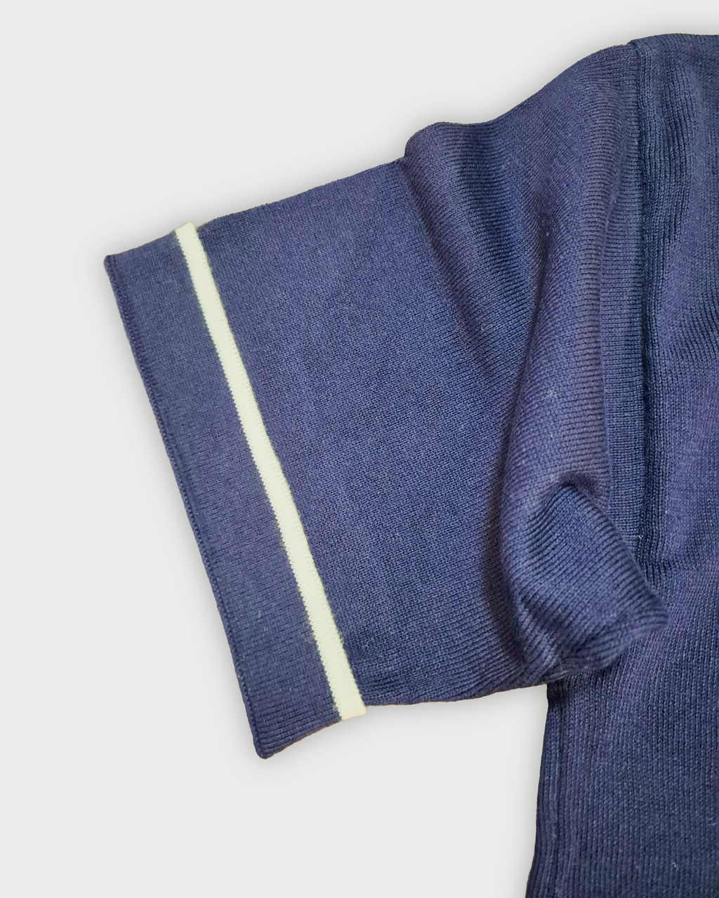 Dettaglio della manica con bordino bianco della polo donna over in maglia di cotone blu su sfondo bianco