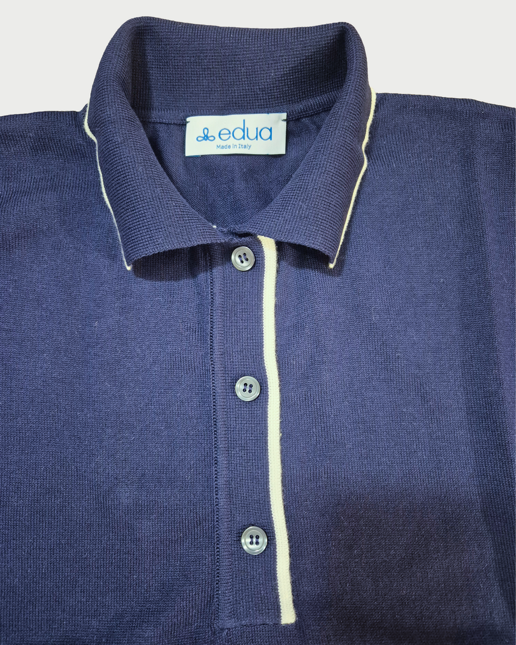 Dettaglio del colletto con bordini bianchi della polo donna over in maglia di cotone blu su sfondo bianco