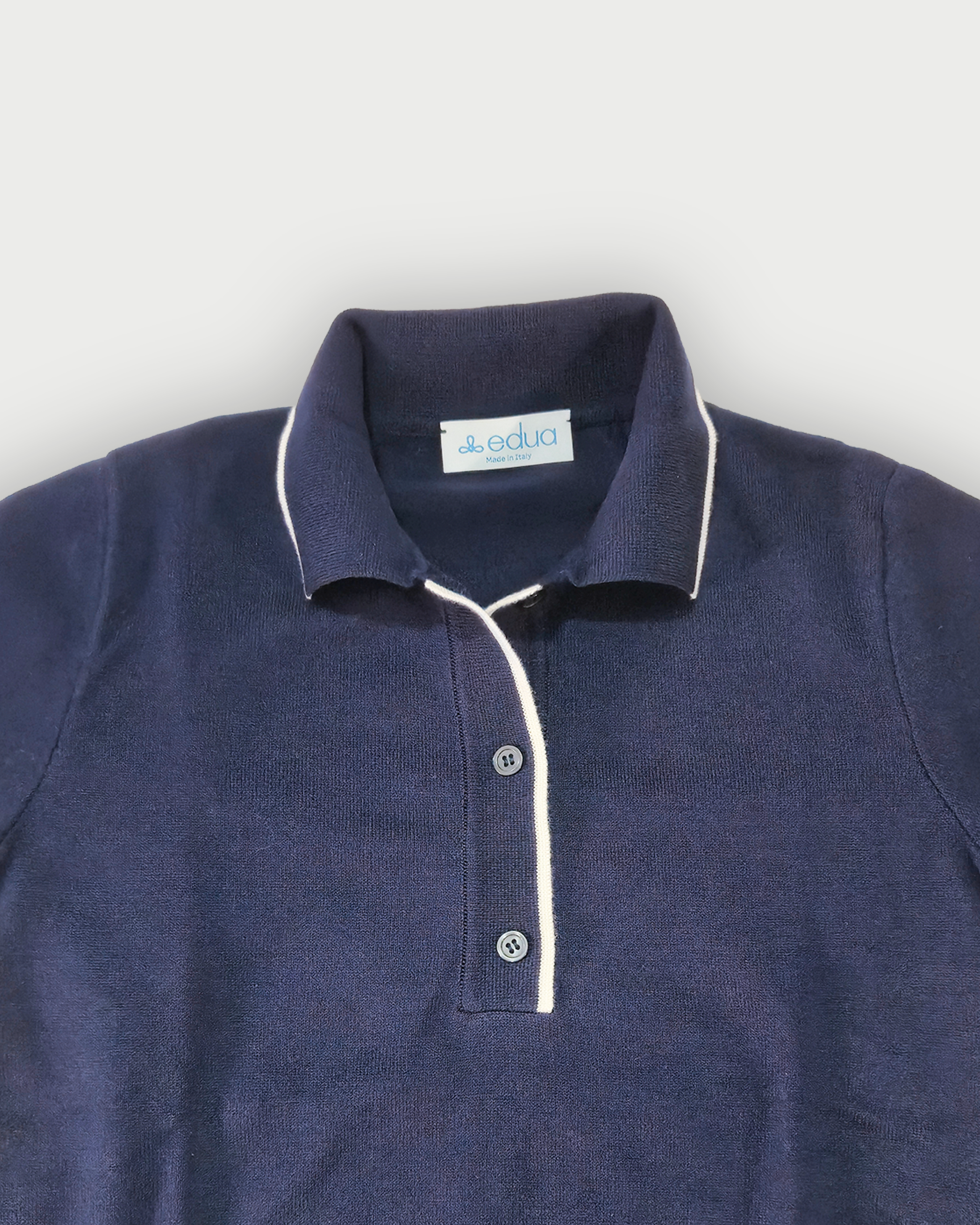 Dettaglio del colletto della polo donna blu con bordi bianchi su sfondo bianco