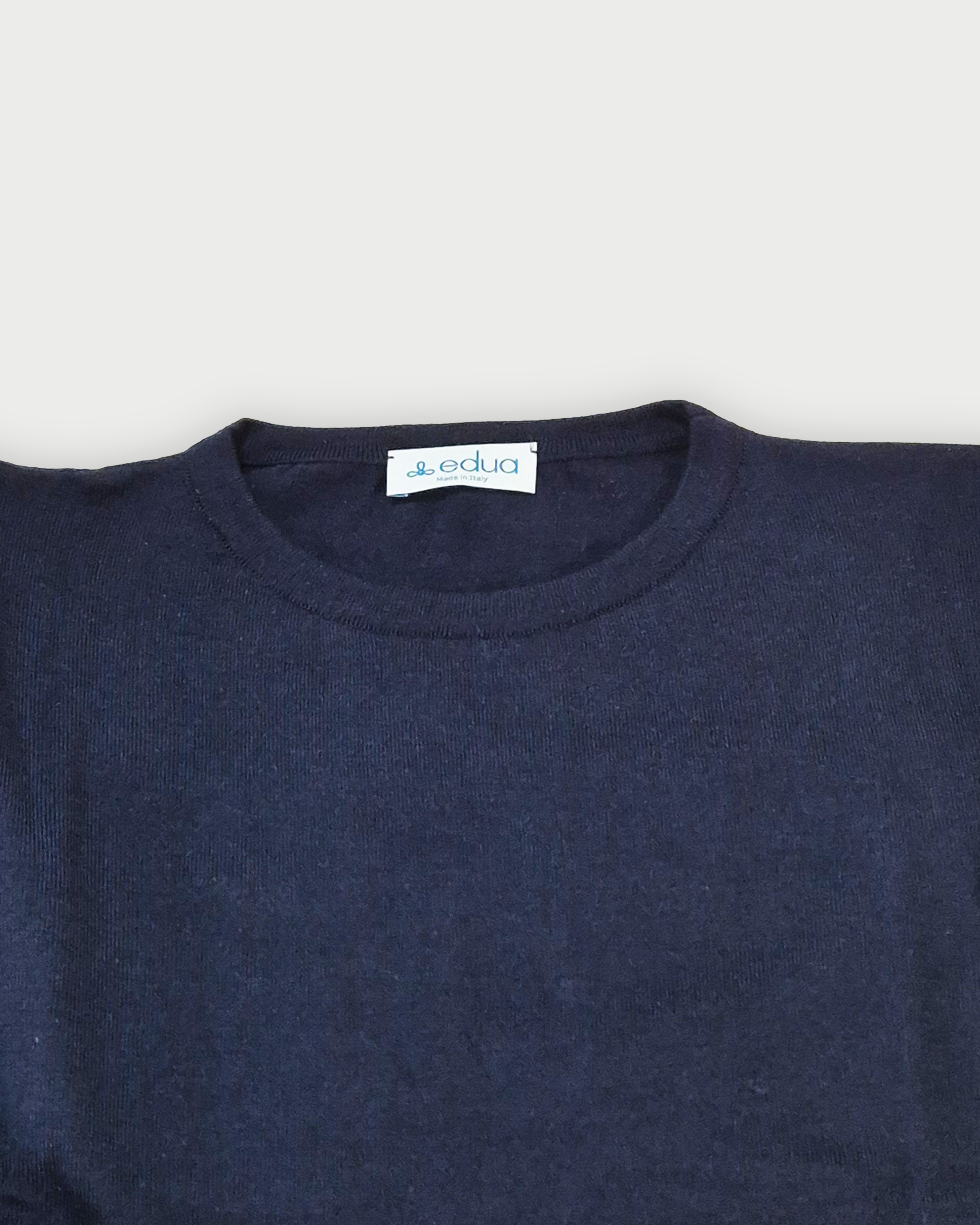 Dettaglio del colletto della maglia donna in maglia di cotone blu con girocollo e profili rossi sulle maniche su sfondo bianco