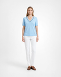 Maglia donna in maglia di cotone celeste con scollo a V e profilo blu indossata su sfondo bianco